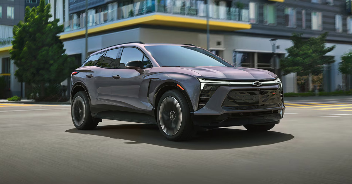 Gray Chevrolet Blazer EV SUV driving on city street, sleek electric crossover design, modern urban background