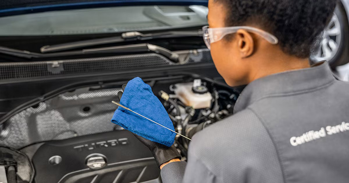 Certified service technician checking oil level in Chevrolet engine, blue microfiber cloth and dipstick visible at Beck Motors Sunnyside