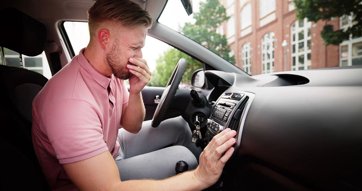Man sitting in car holding his nose